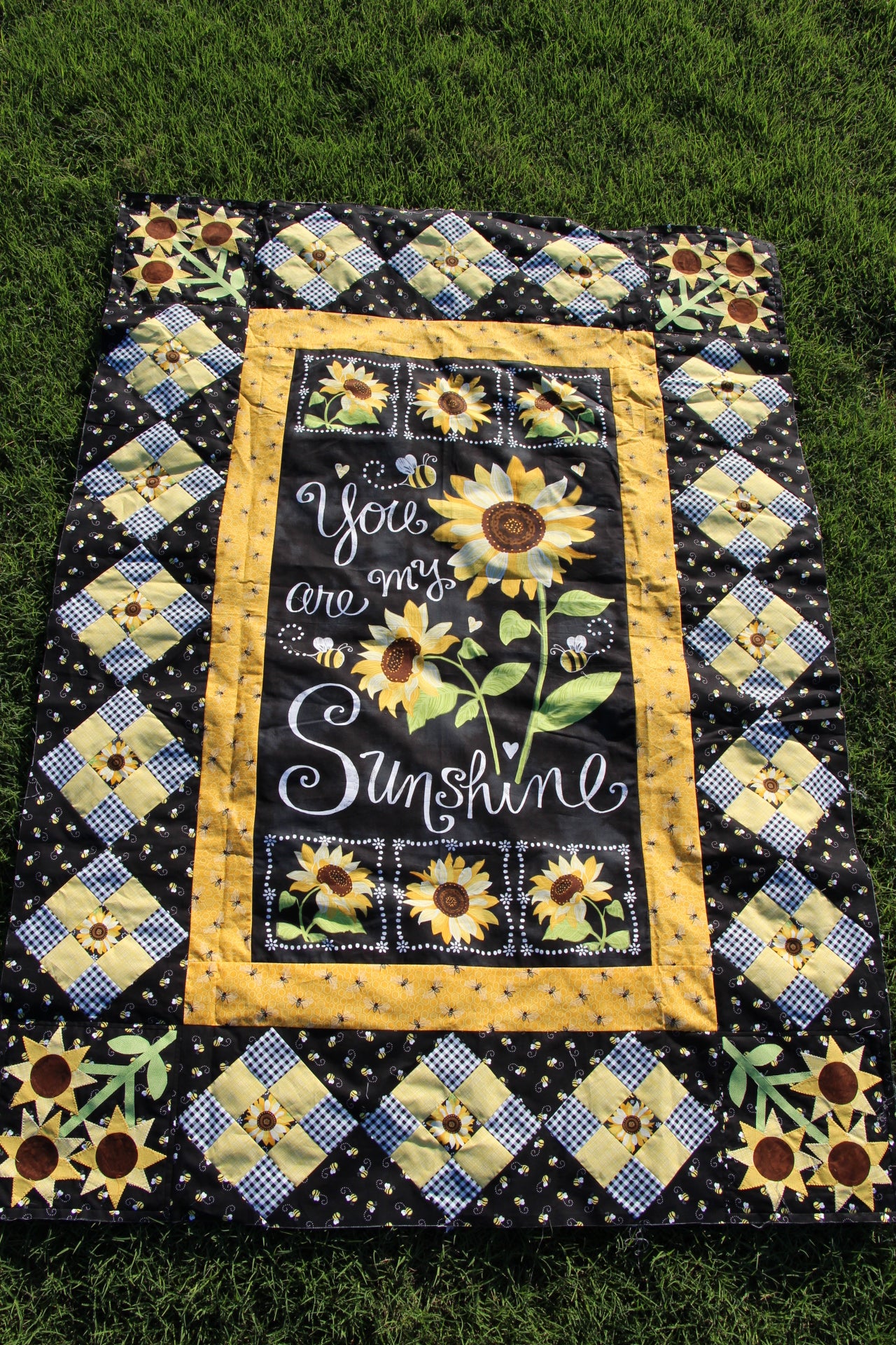 Sunshine All Around You quilt top. Middle features the You Are My Sunshine chalkboard fabric panel. Panel surround with nine patch square set on point and sunflower applique.