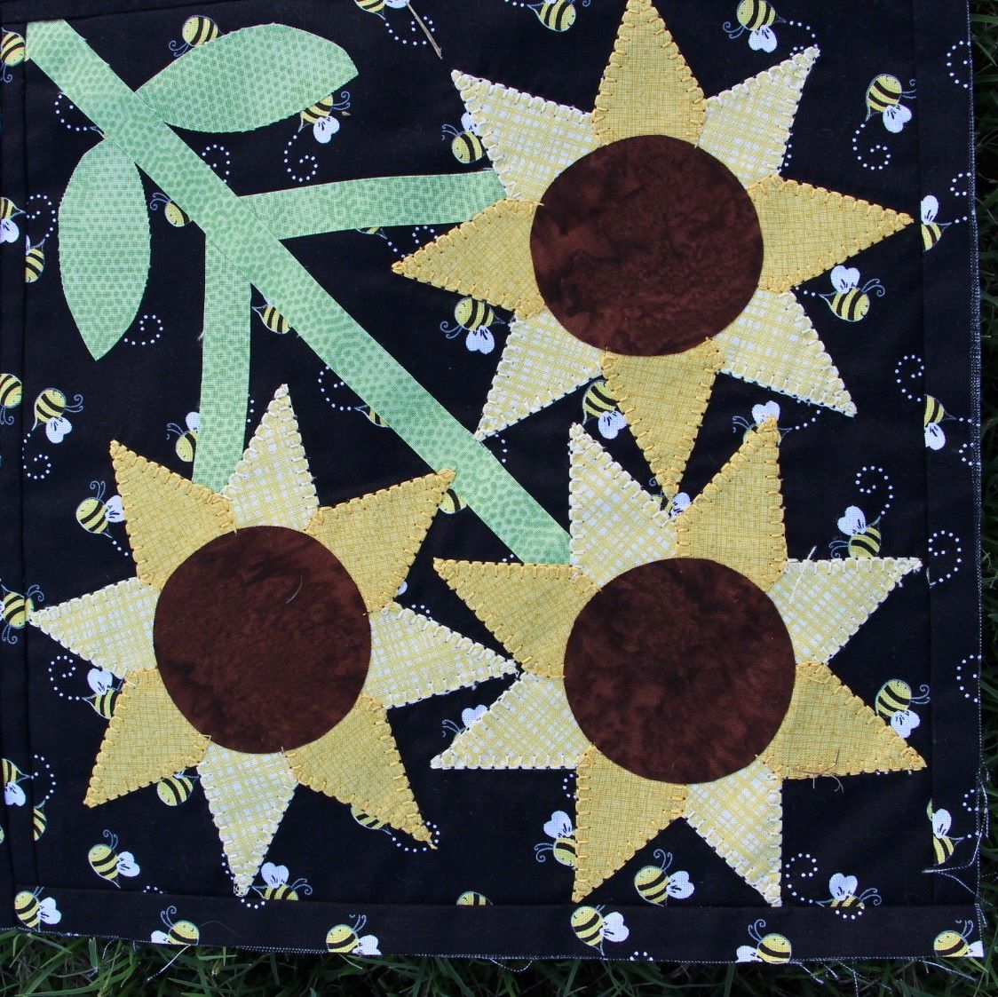 Close-up photo of the fusible applique sunflowers on bee fabric.  The fusible applique is outlined with a blanket stitch to provide definition to the flowers.